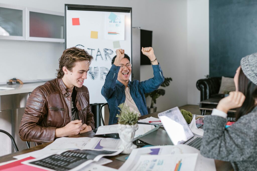 A group of diverse colleagues joyfully celebrate a successful meeting in a modern office setting.